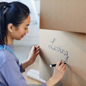 Girl writing the words living room on moving box