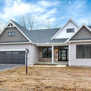 A newly constructed single-family home with the porch light on surrounded by trees.