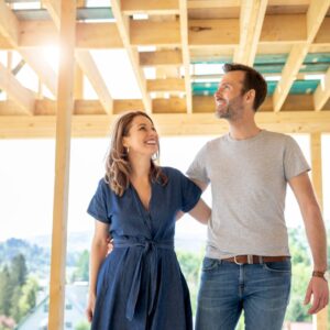 A husband and wife smiling and looking at the framing of their new construction home.